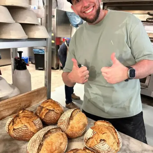 Robbert met duimen omhoog in een professionele bakkerij, omringd door zuurdesembrood