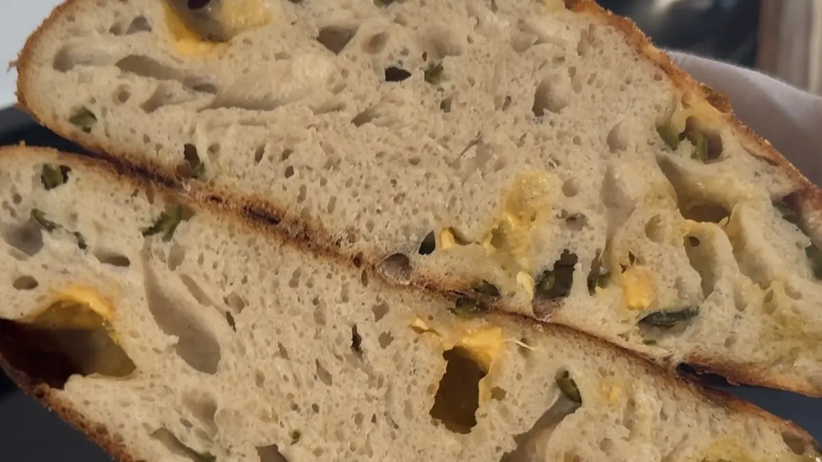 Doorgesneden cheddar-jalapeño zuurdesembrood met zichtbare kaas-pockets en jalapeño in de kruim