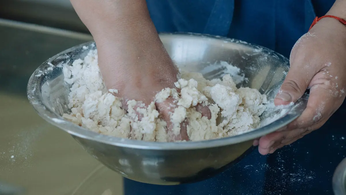 Handen mengen deeg met bloem en water in een kom